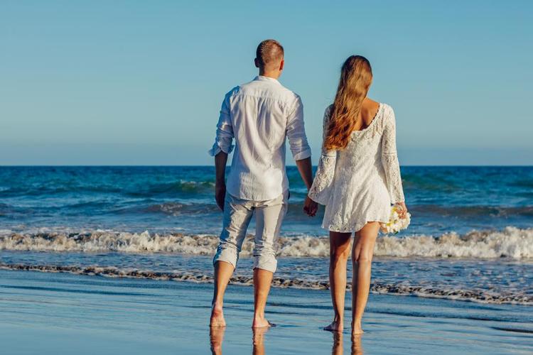 蓝白人物温馨在海滩边牵手行走的男女情侣自然旅游休闲背景图片